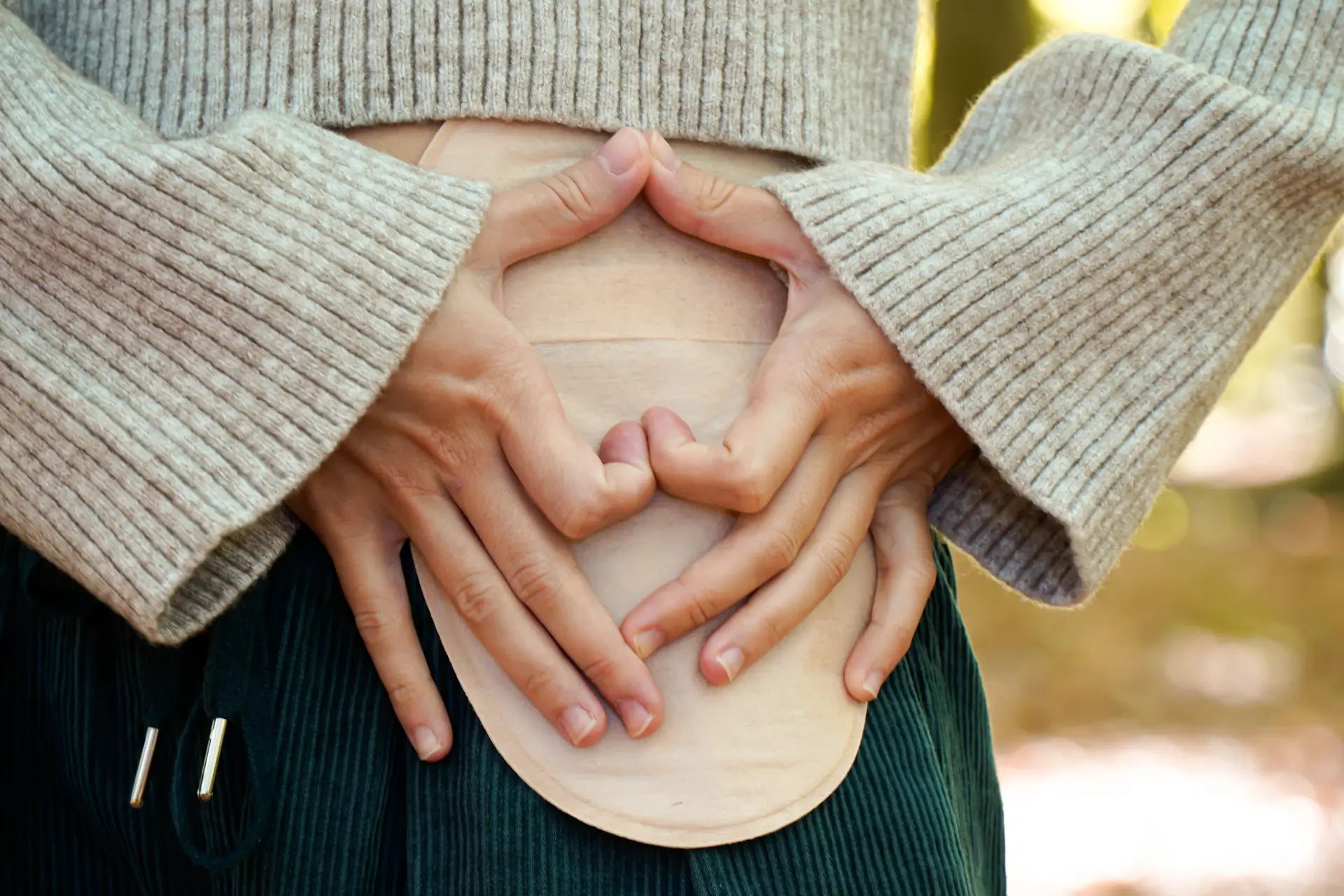 Girl forming a heart shape with her hands over her ostomy pouch on her abdomen