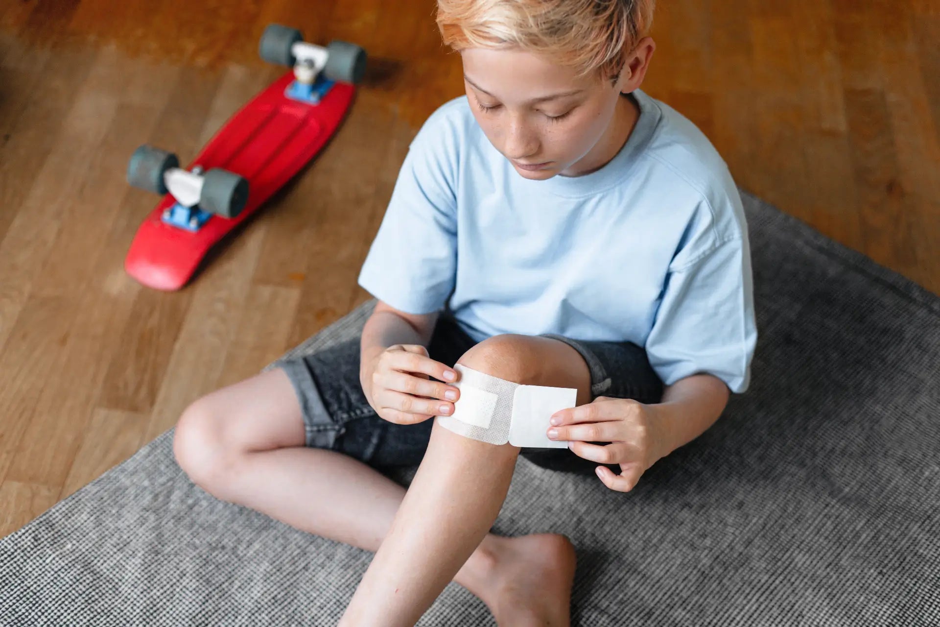 Boy independently applying a nonwoven wound dressing to his injury